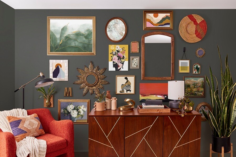 Sala de estar con pared oscura, arte enmarcado y espejos colgados con tiras Command. Un aparador de madera, sillón rojo y planta alta completan la decoración chic.
