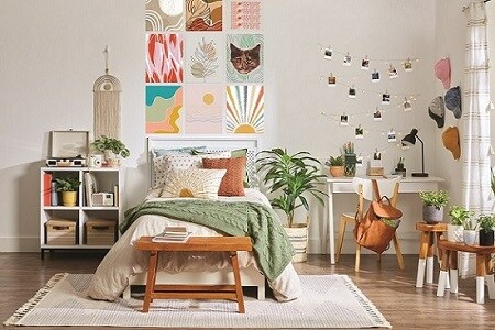Dormitorio acogedor con cama bien hecha, almohadas y manta verde. Impresiones artísticas sobre la cama con tiras Command. Escritorio, silla y fotos con ganchos Command añaden encanto. Plantas aumentan calidez
